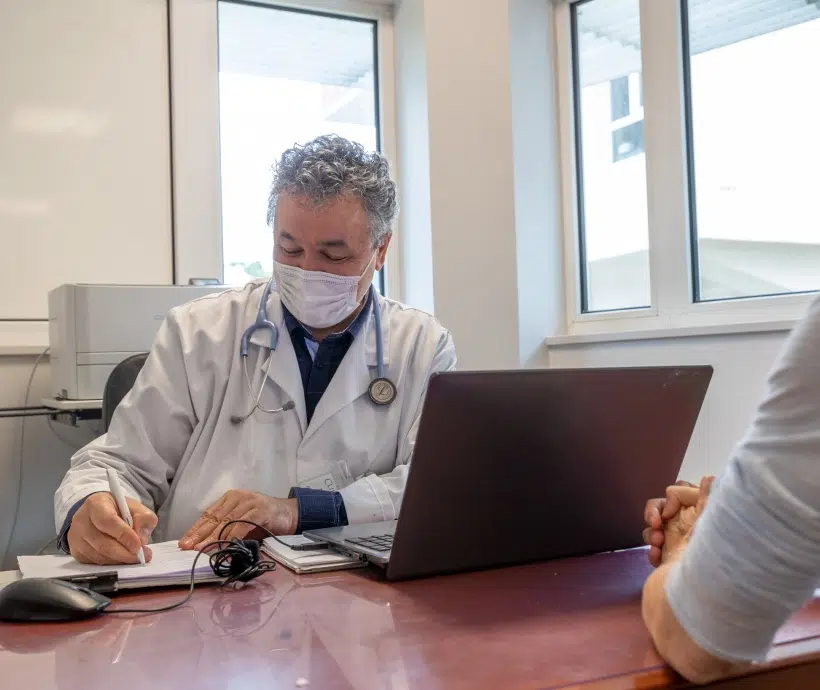 Médecin écrivant des notes sur son bureau - la prise en charge cardiovasculaire | Clinalliance Paris