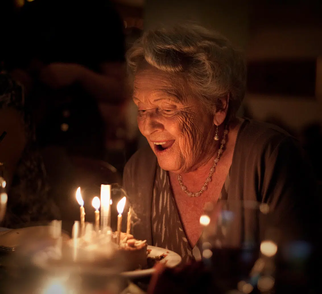 Femme agée souflant sur des bougie sur un gâteau d'anniversaire | Clinalliance Paris