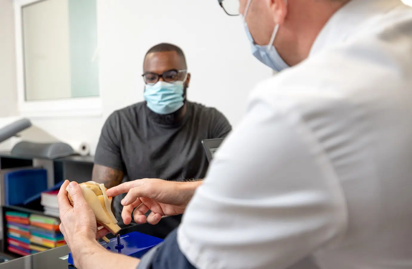 Médecin tenant un modèle de mâchoire parlant avec un homme | Les postes a pourvoir | Clinalliance Étampes