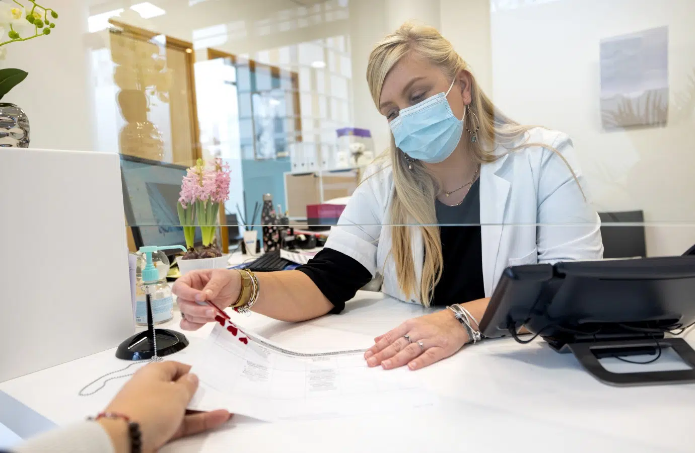 Docteur assise à un bureau tient un document qu'elle remet à une patiente - les postes à pourvoir | Clinalliance Pierrefitte