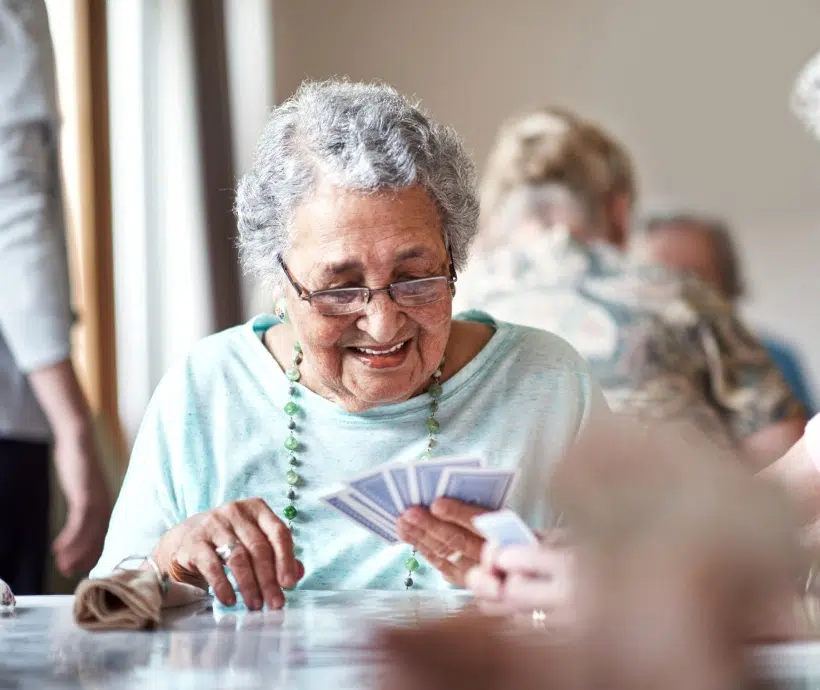 Femme âgée joue aux cartes à une table - jeux de société | Clinalliance Paris